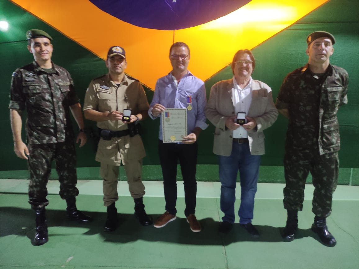 Imagem com bandeira do Brasil ao fundo e na frete cinco pessoas mostram homenagens recebidas pelo exército