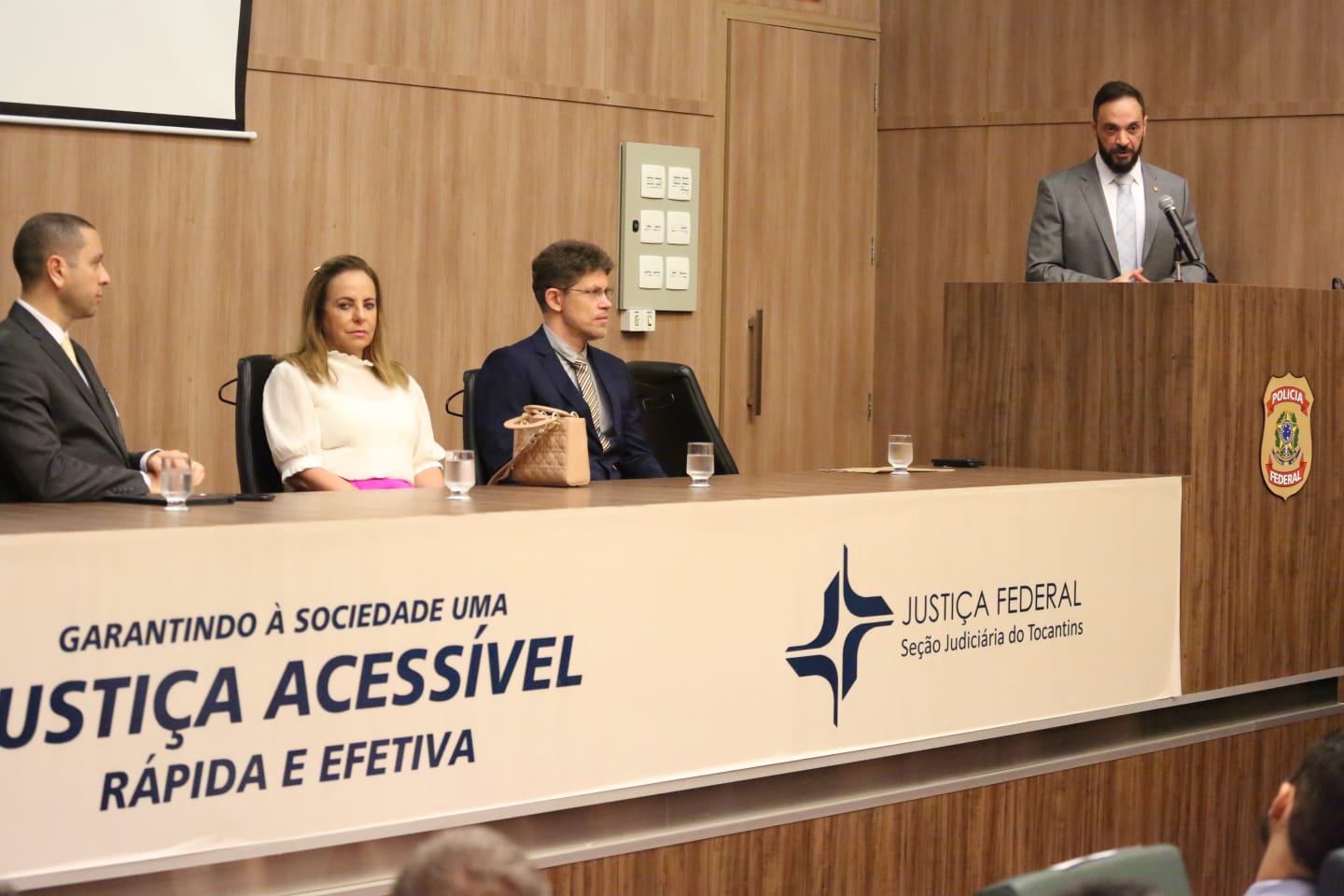 Novo superintendente discursando com a vice-presidente do TJTO e o procurador-chefe do MPF/TO compondo a mesa 