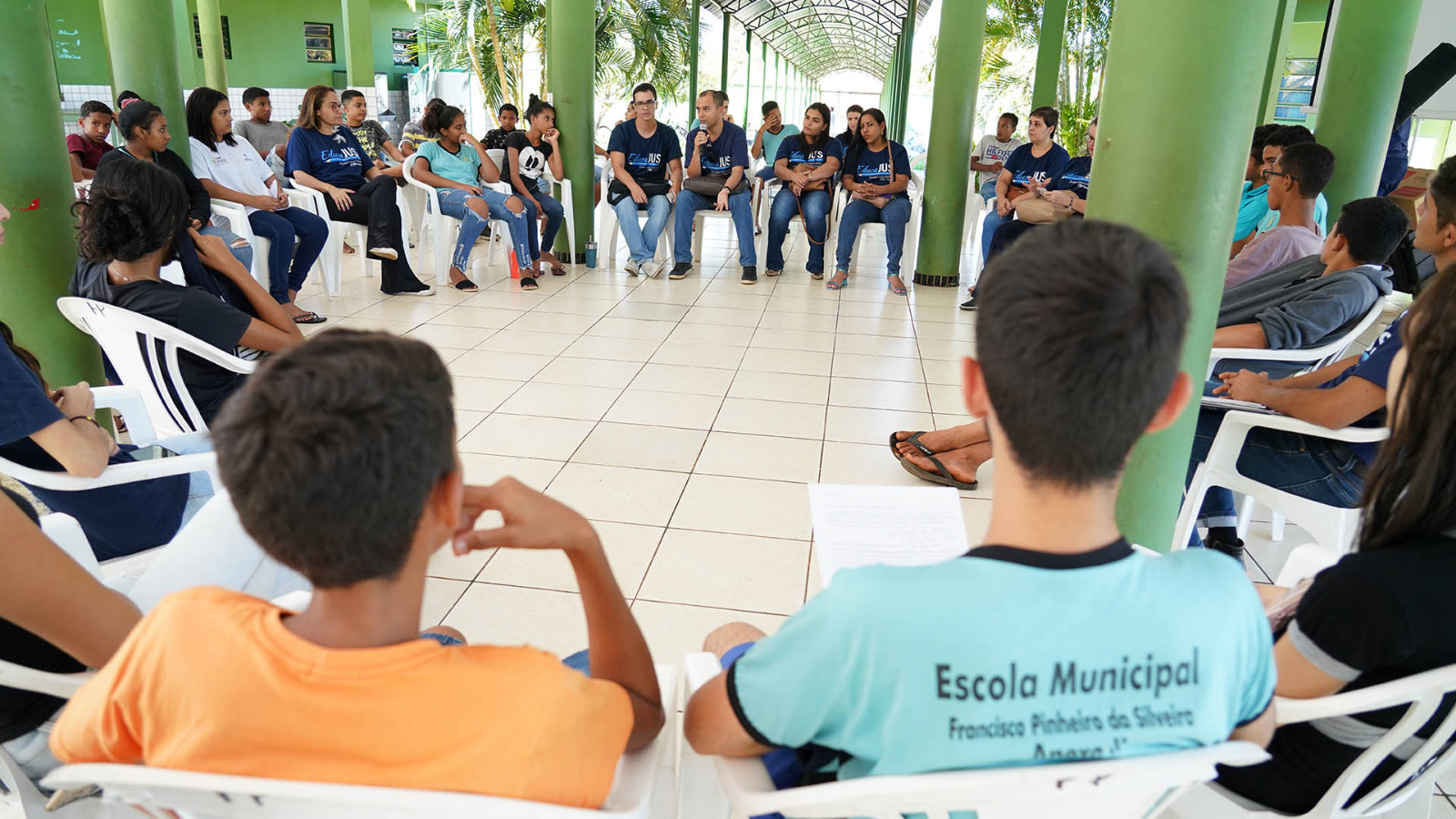 Imagem colorida de adultos e jovens sentados em roda num pátio 