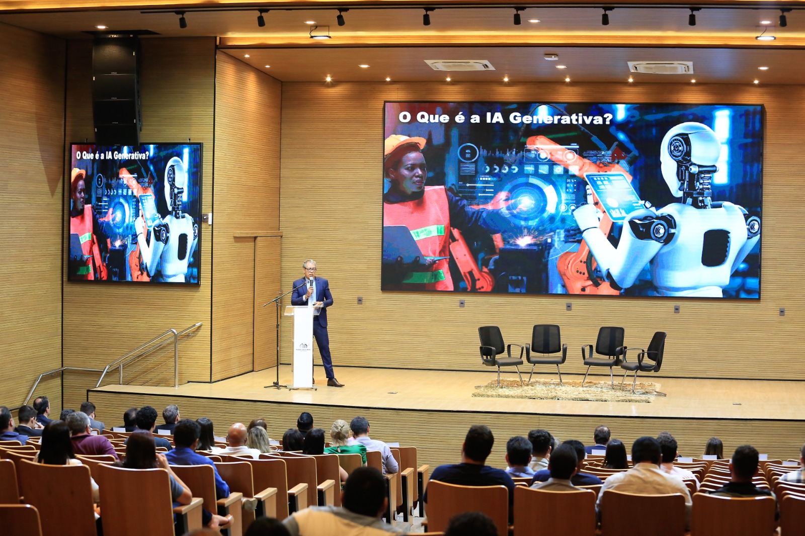 Palestra em auditório com homem palestrando em pé no púlpito, ao fundo telão em led colorida 