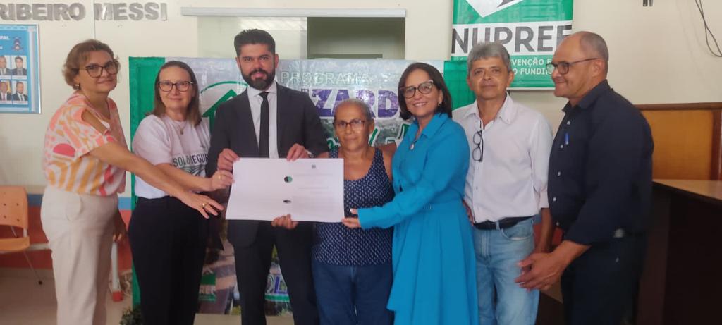 Foto com sete pessoas em pé segurando um documento que traz título de propriedade rural