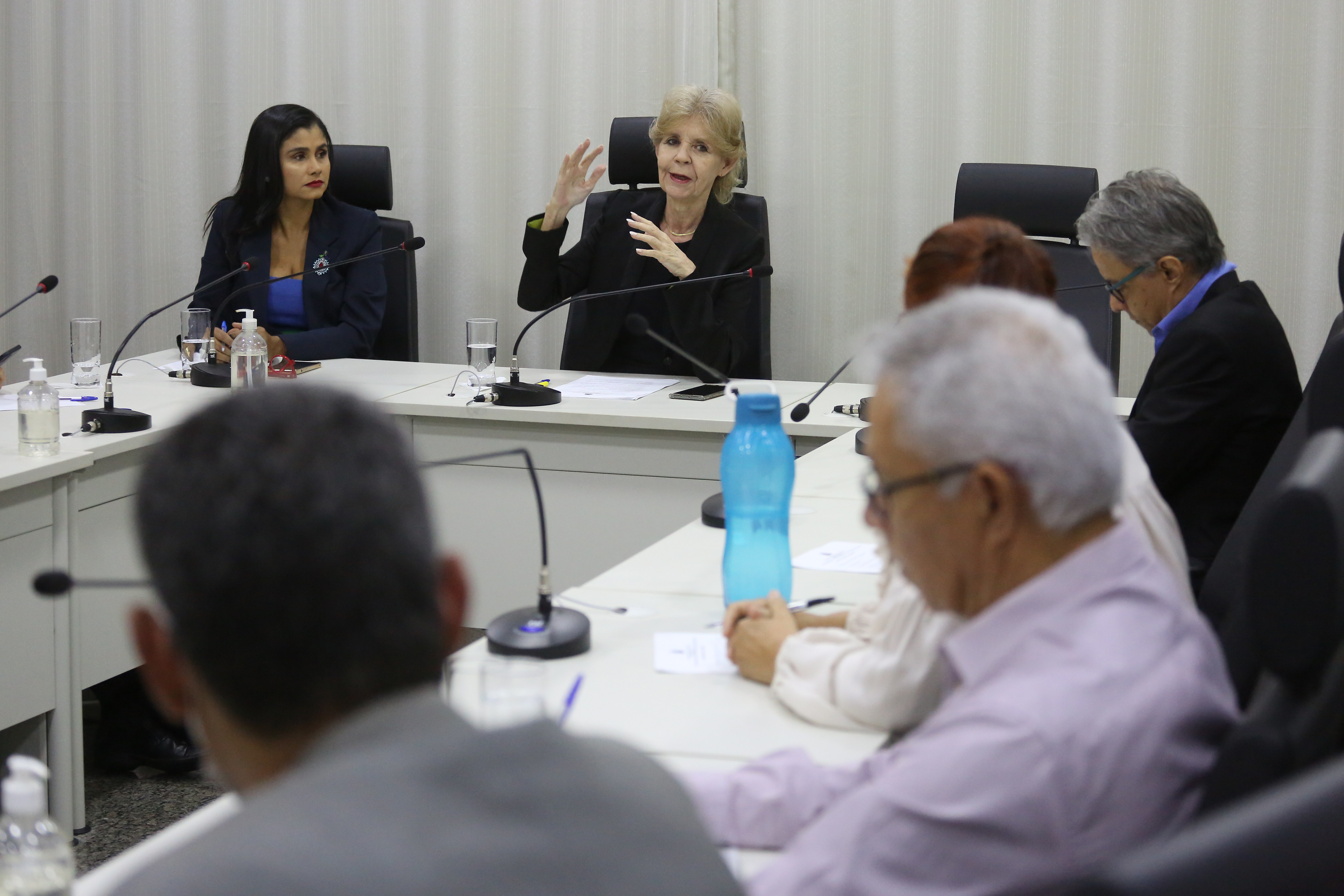 Homens e mulheres sentados em volta de uma mesa em U de cor branca durante reunião