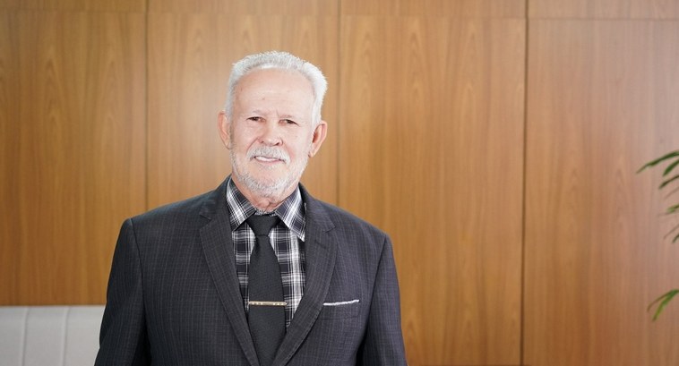 Foto posada de senhor branco, de cabelos e barba brancas, trajado de camisa xadrez preta e branca, gravata e terno cinza escuro