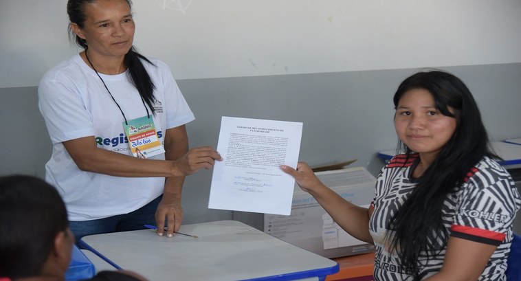 Jovem indígena recebendo novo registro civil pelas mãos de uma voluntária da ação