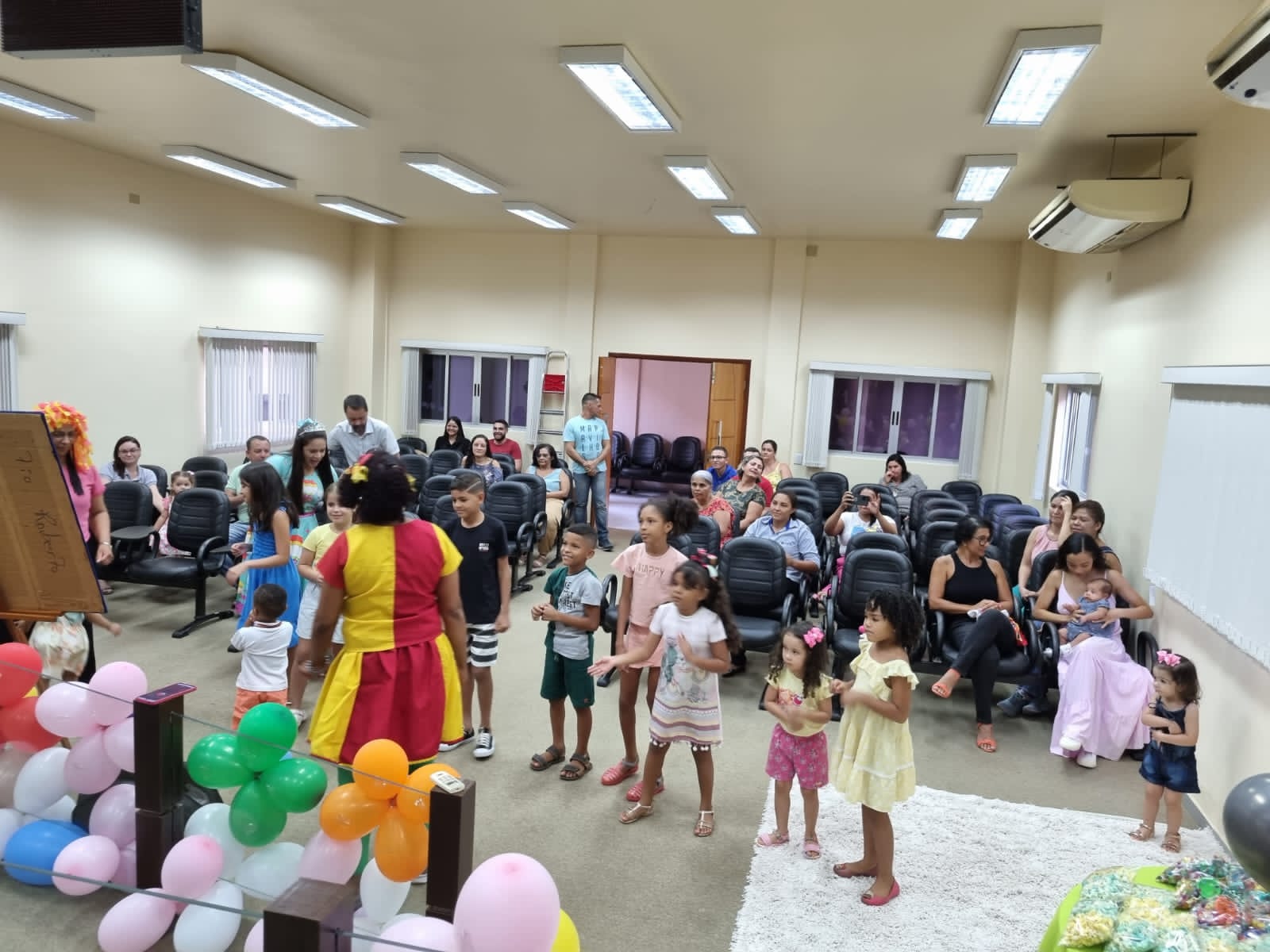 crianças reunidas olhando atentamente a uma mulher vestida de palhaço