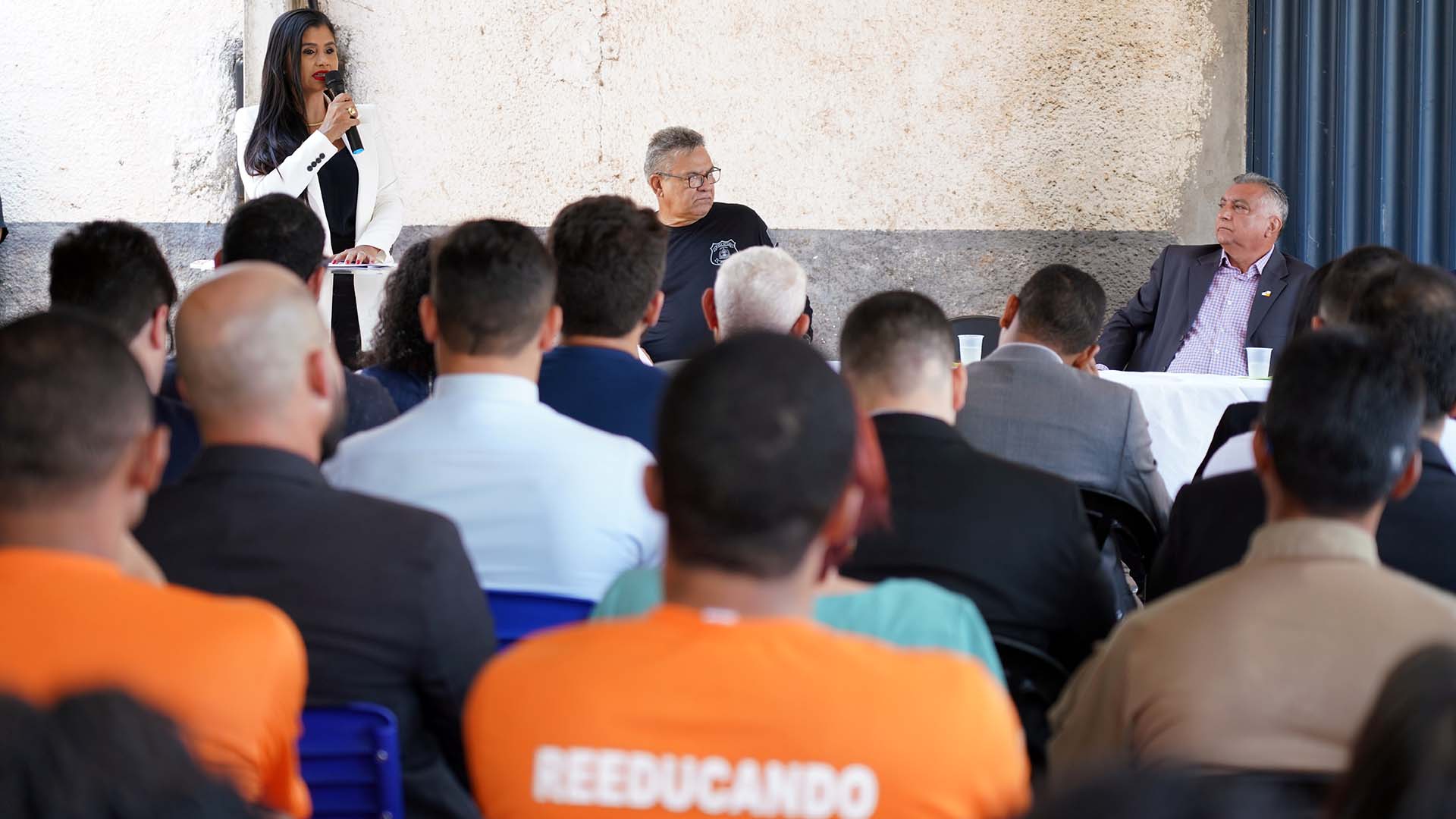 Mulher morena usando branco e preto fala para homens sentados na plateia