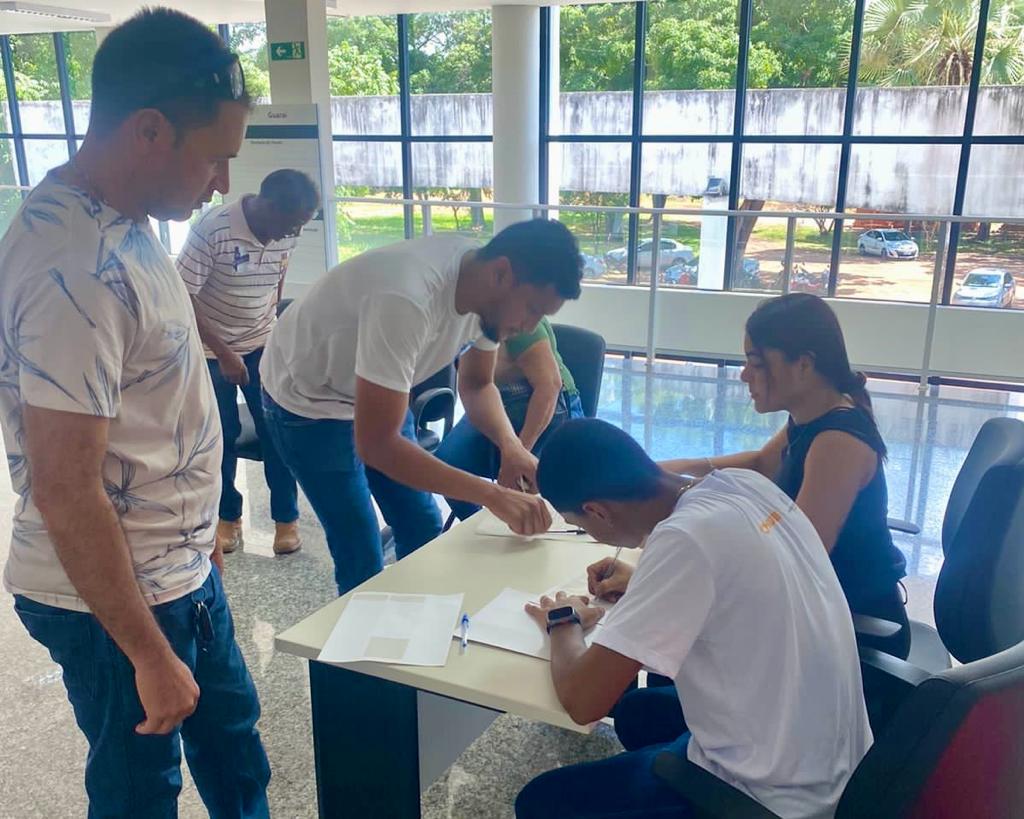 Homens assinam documento em frente à mesa