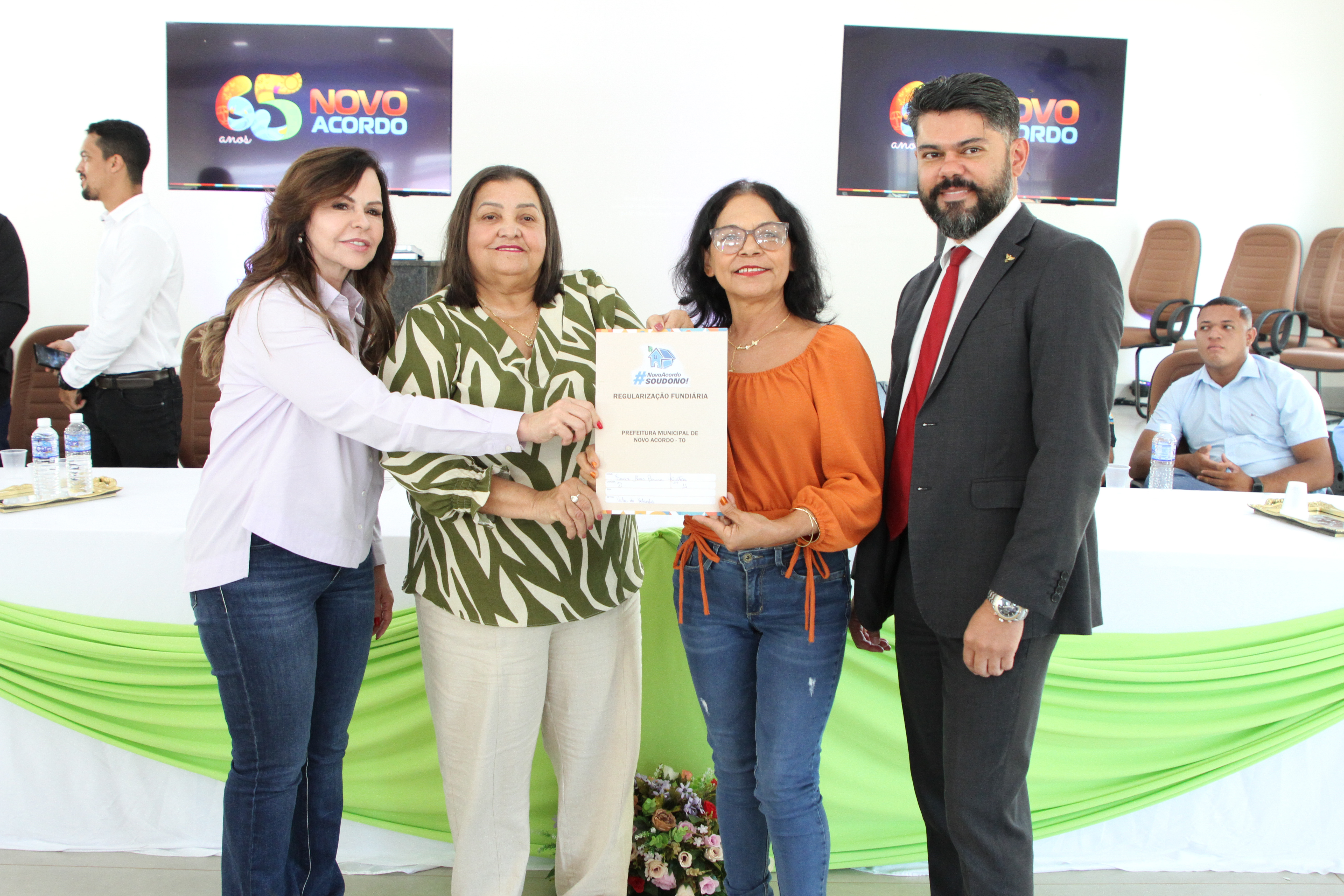 mulher beneficiada posa ao lado de magistrados e servidores segurando a escritura