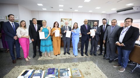 Fotografia colorida que mostram homens e mulheres posando para a imagem e segurando um documento nas mãos.