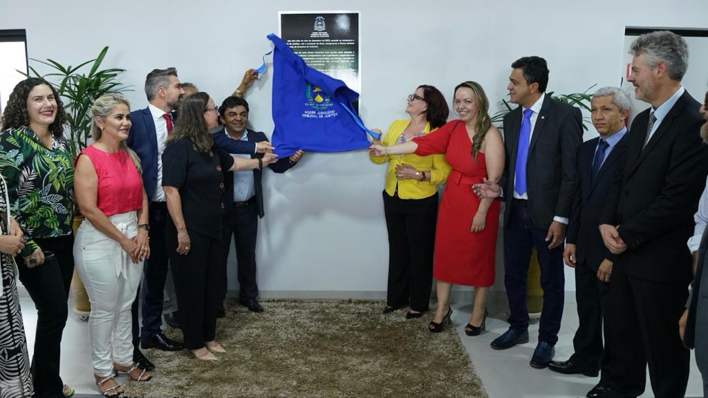Fotografia colorida que mostra homens e mulheres descerrando a placa inaugural do Fórum da Comarca de Colméia. A desembargadora Etelvina Maria segura o tecido em primeiro plano. 