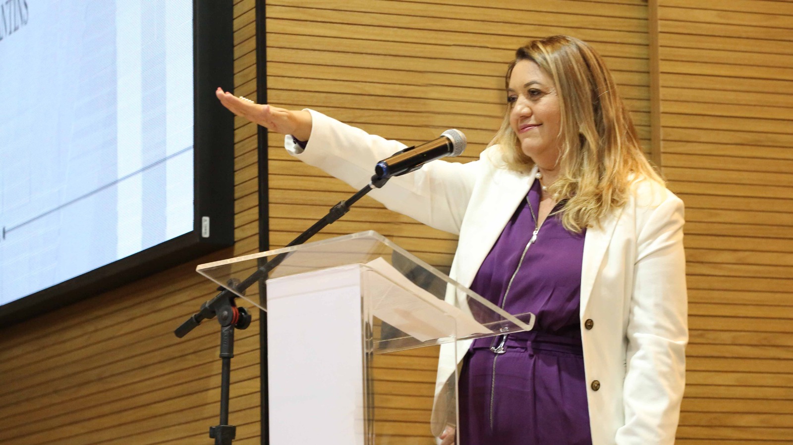 Nova delegatária com braço levantado em alusão ao juramento e falando ao microfone