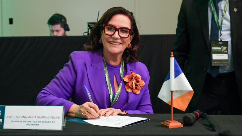 Imagem mostra a presidente do TJTO com roupa lilás assinando um documento