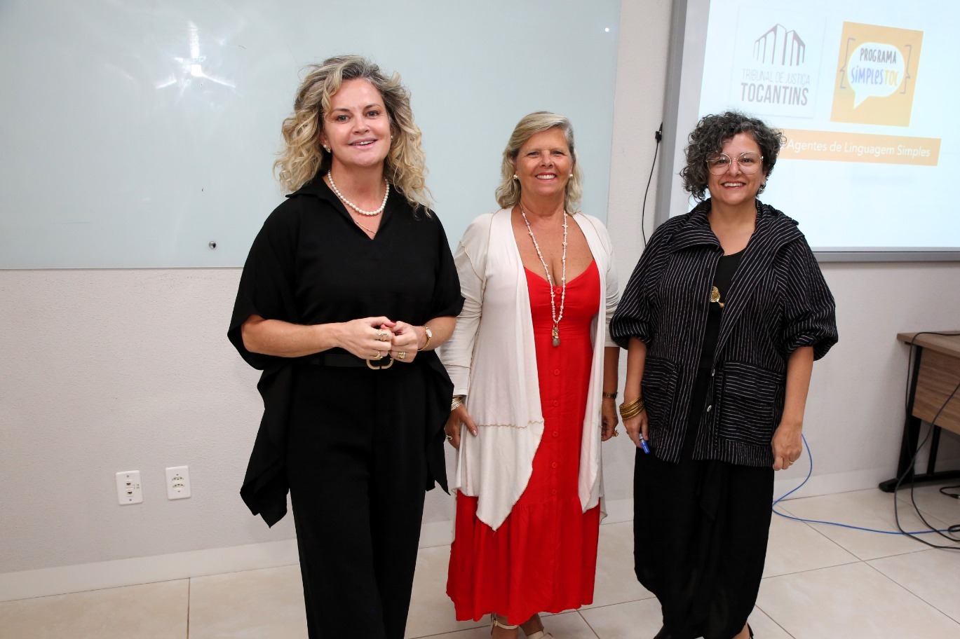 Imagem colorida de tres mulheres posando para foto numa sala de aula