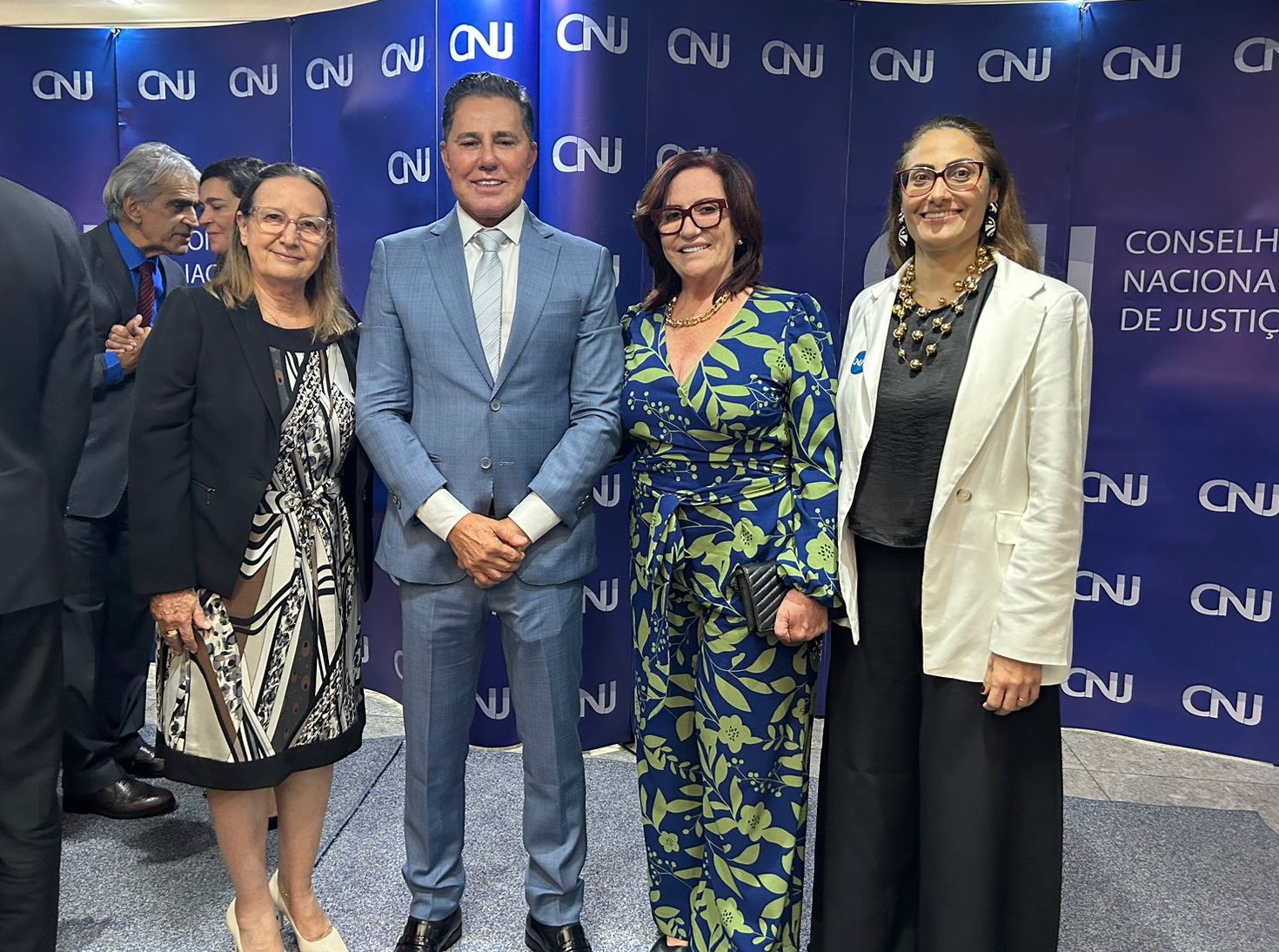Fotografia colorida da Presidente do Tribunal de justiça do Tocantins, desembargadora Etelvina Maria Sampaio Felipe, ao lado da Corregedora Geral do TJTO desembargadora Maysa Vendramini Rosal, o  Desembargador José Rotondano e a juíza auxiliar da Presidência, Rosa Maria Gazire Rossi. Eles estão posando em pé para a foto, em frente a um banner grande azul na parede com os dizeres CNJ