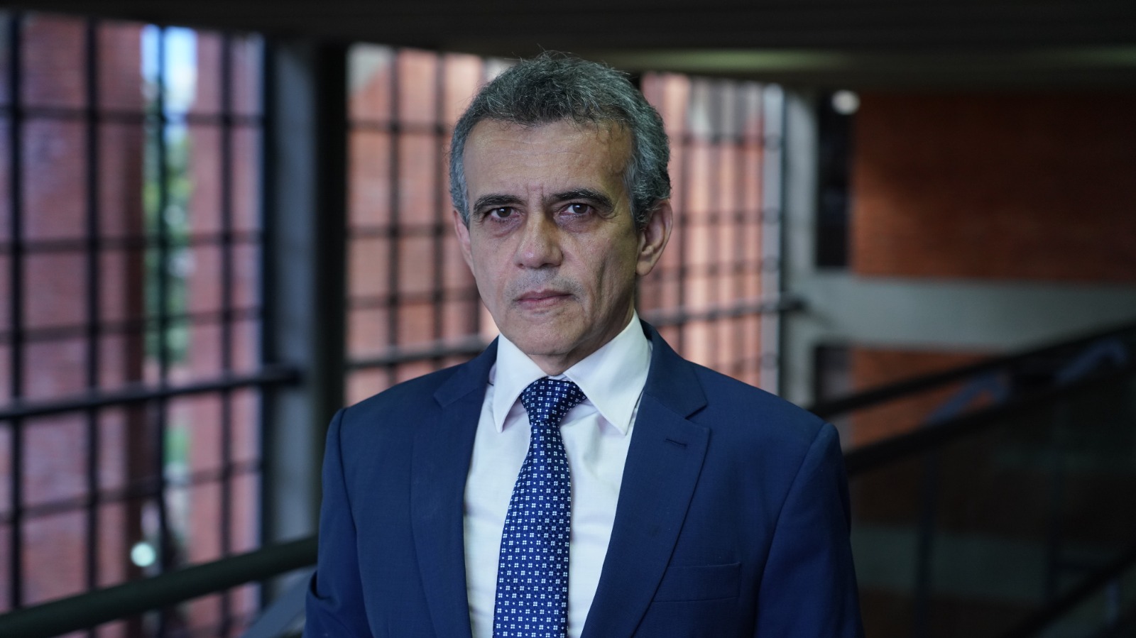 Juiz Allan Martins, nas dependêcias do Tribunal de Justiça; homem com cabelos grisalhos, usa camisa branca, terno e gravata azul 