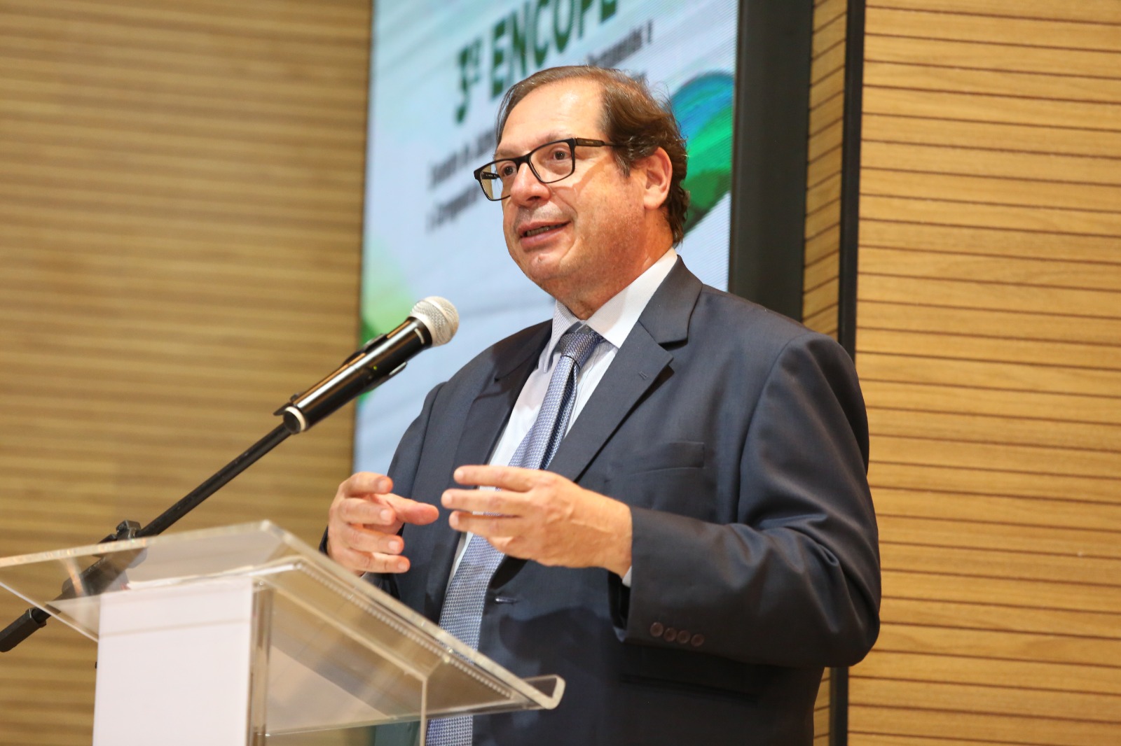 Fotografia colorida do corregedor nacional de justiça, ministro Luis Felipe Salomão falando em um microfone, de frente a um palanque de vidro, vestindo terno e gravata 