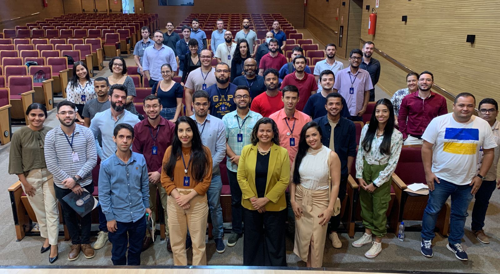 Kézia Reis, de roupa preta e blazer mostarda, em pé com os servidores, no auditório do TJ