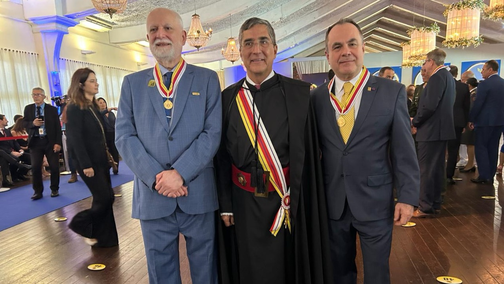 Foto com três homens brancos, com ternos escuros em pé olhando para frente