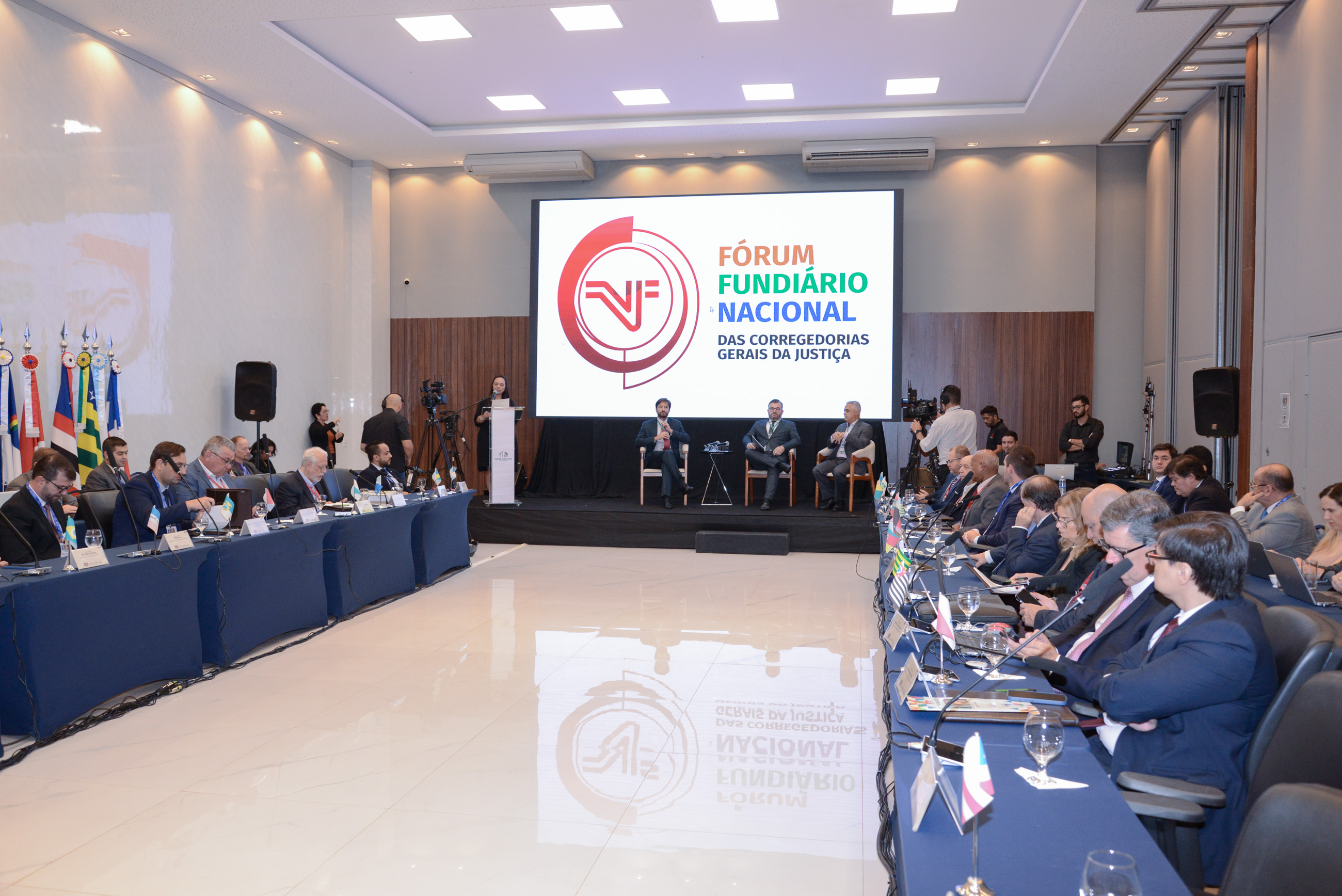 Fotografia colorida com diversas autoridades em uma sala durante o Fórum Fundiário Nacional