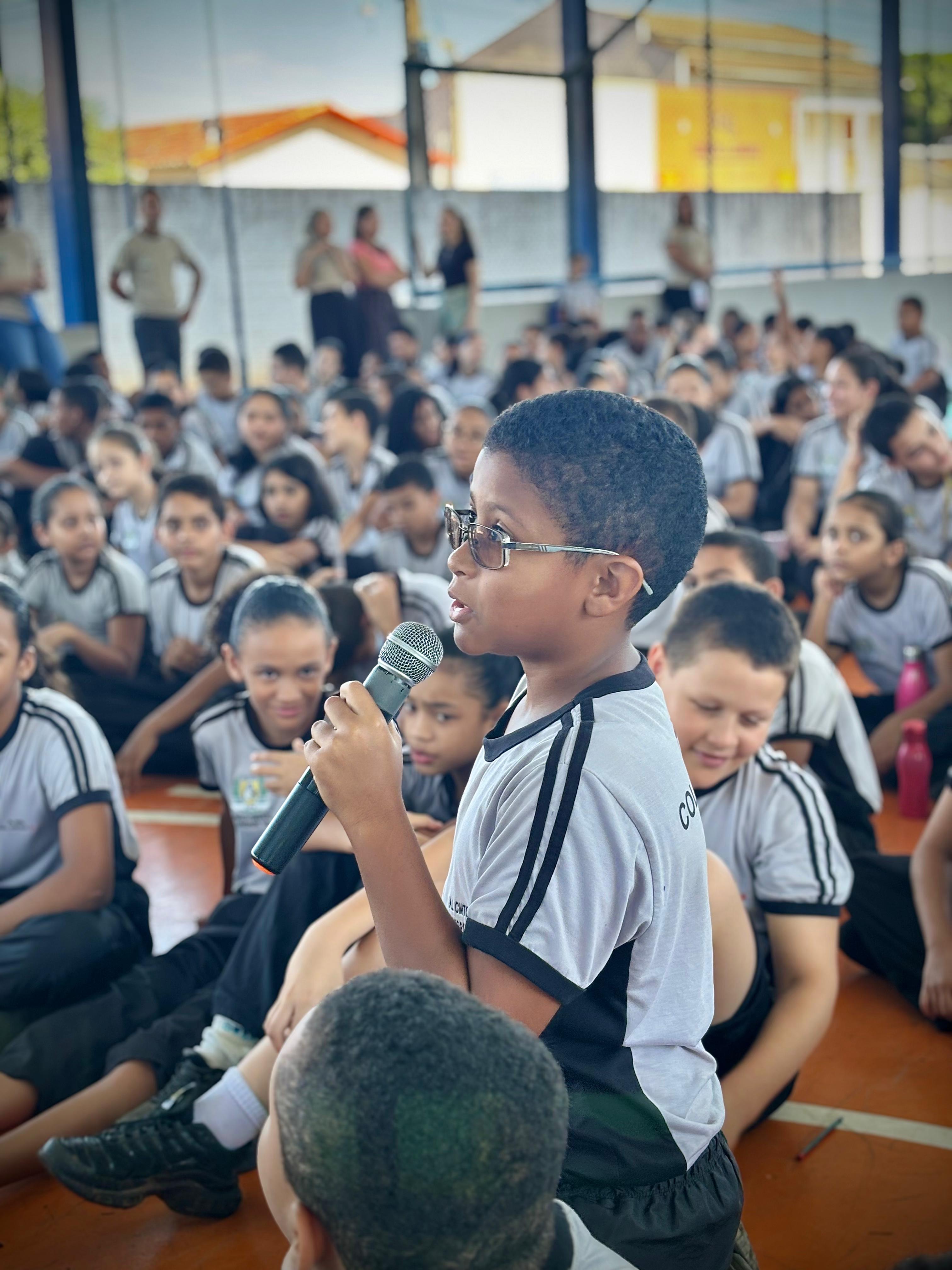 uma criança falando ao microfone ao lado de outras várias, todas uniformizadas, durante palestra