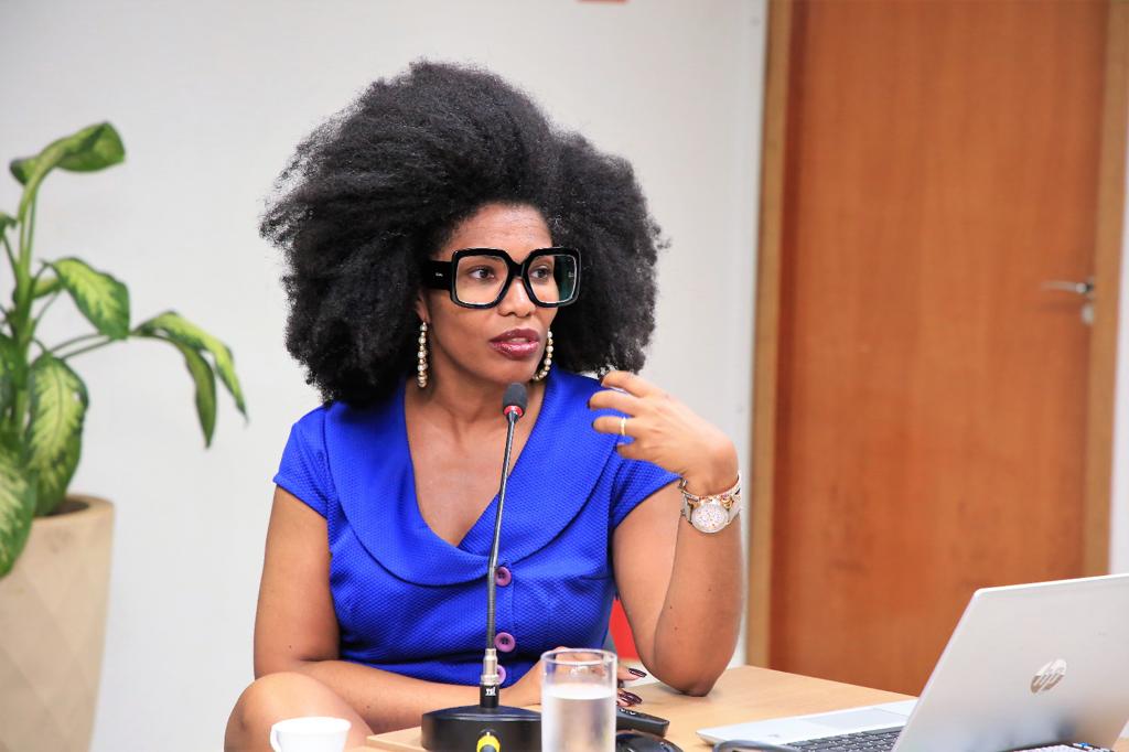 Fotografia colorida que mostra uma mulher negra vestindo azul, falando ao microfone