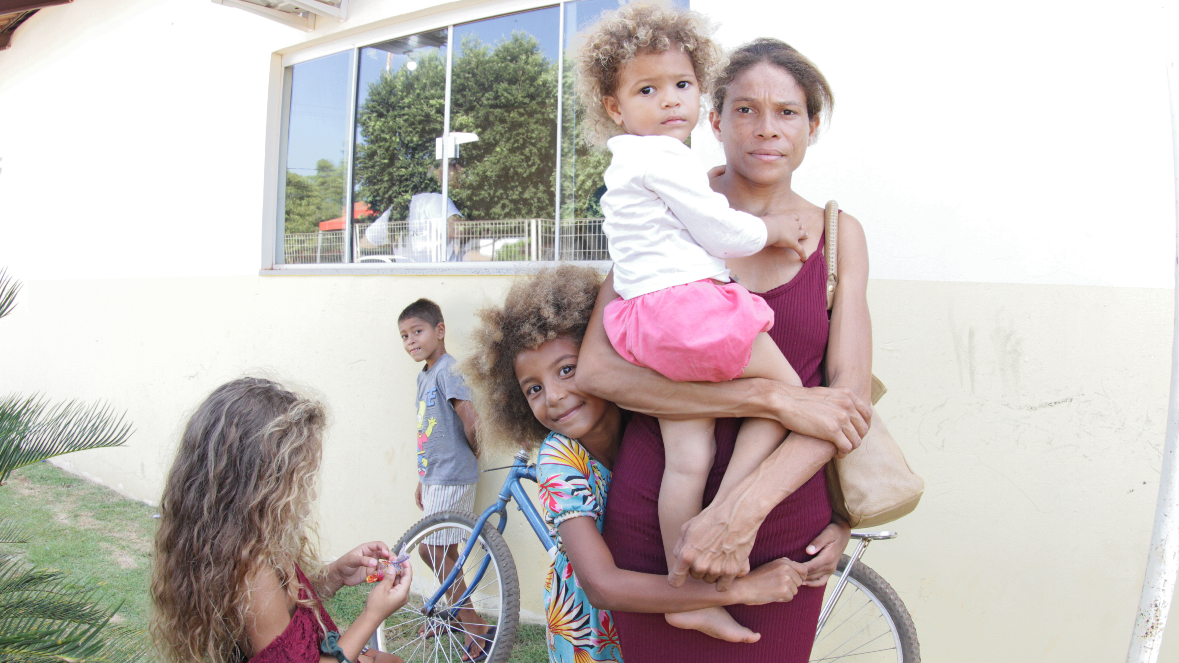 Fotografia colorida que mostra uma mulher morena segurando uma criança no colo e com outras duas crianças abraçando-a