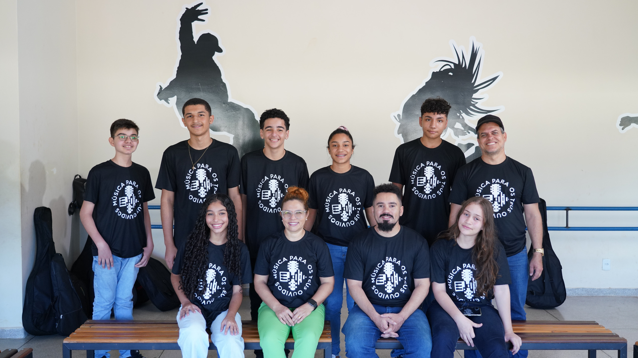 Pessoas usando calça e blusa preta, sentadas e em pé olhando para a foto