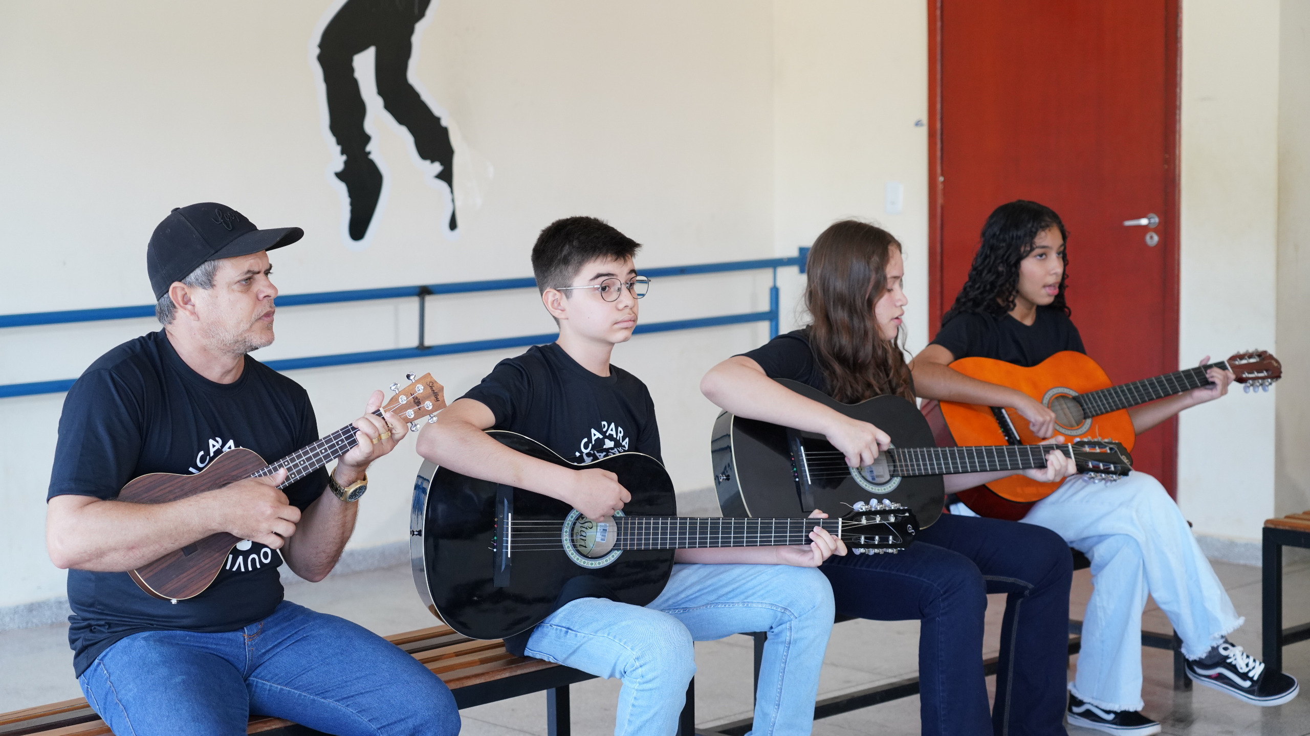 Imagem mostra pessoas vestidas de calça e blusa preta segurando violões