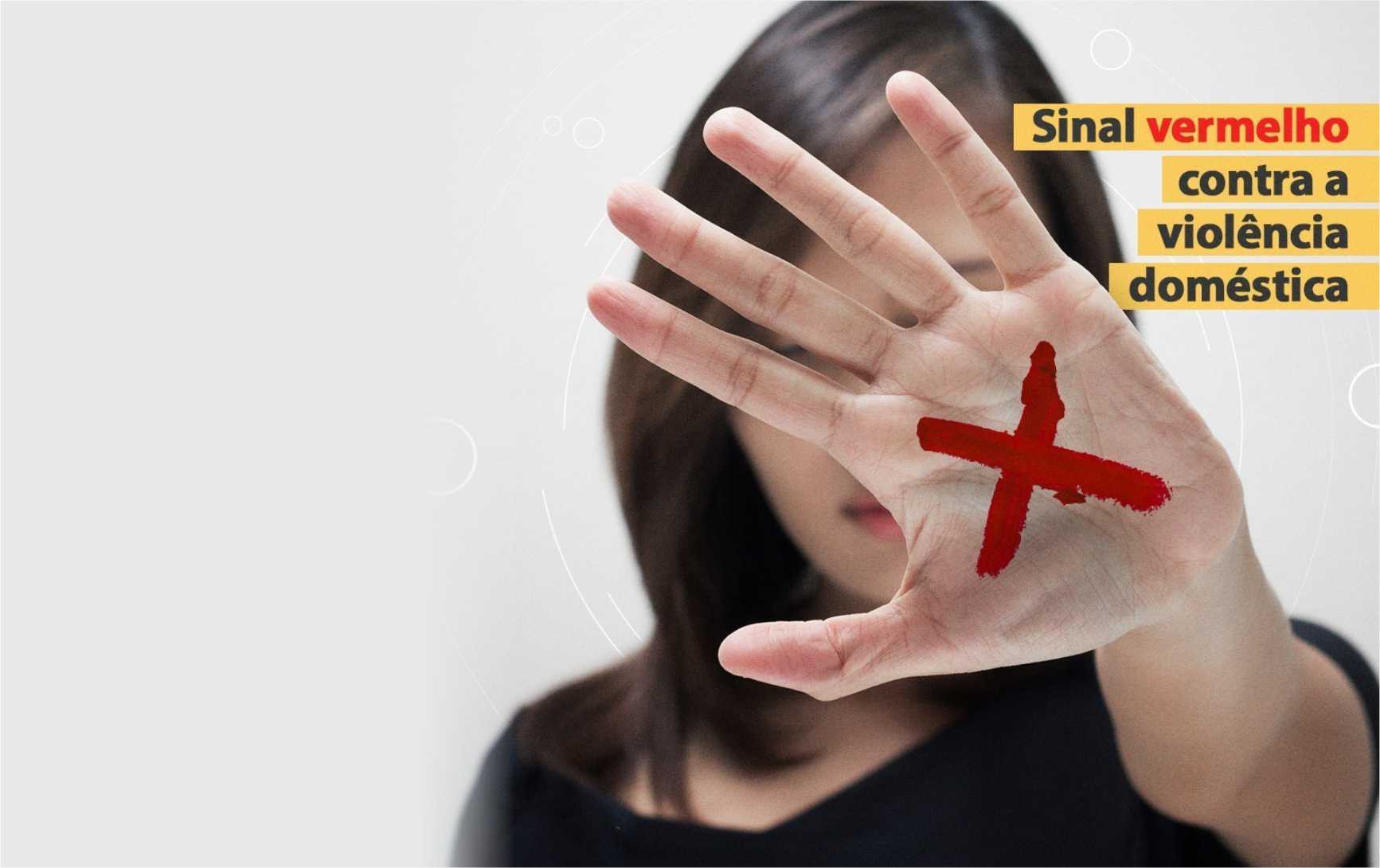 Imagem ilustrativa de uma mulher com o rosto tapado pela mão. Na mão, há um X em vermelho, e está escrito Sinal Vermelho contra a violência doméstica