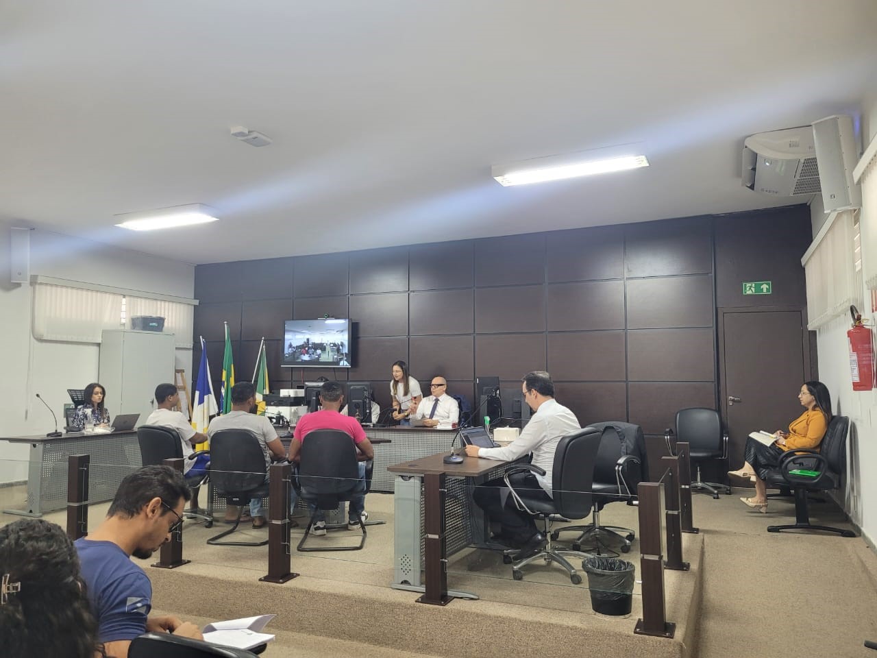 Imagem colorida que mostra homens e mulheres em uma sala de tribunal de júri durante uma audiência concentrada