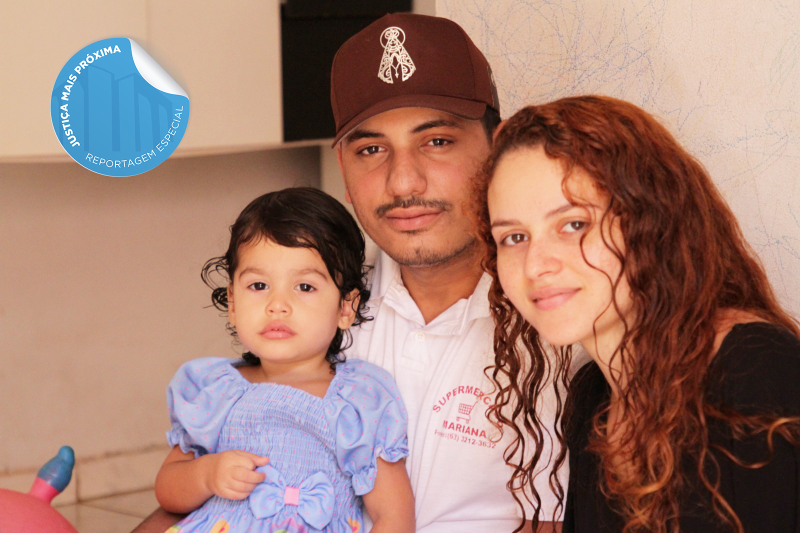 Fotografia colorida que mostra um homem de boné marrom e camisa rosa, com uma menina no colo que usa vestido lilás e ao lado de uma mulher ruiva de cabelos longos e encaracolados. Eles formam uma família, em cima da imagem há um selo azul escrito:"matéria especial"