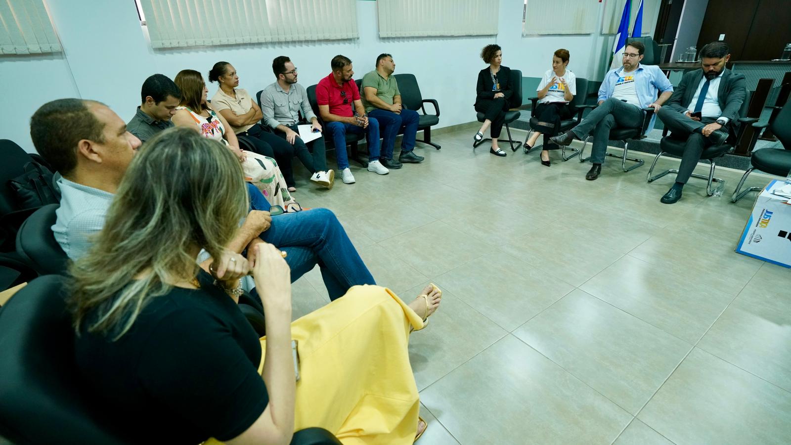 Várias pessoas sentadas em uma sala escutam a explicação de uma pessoa