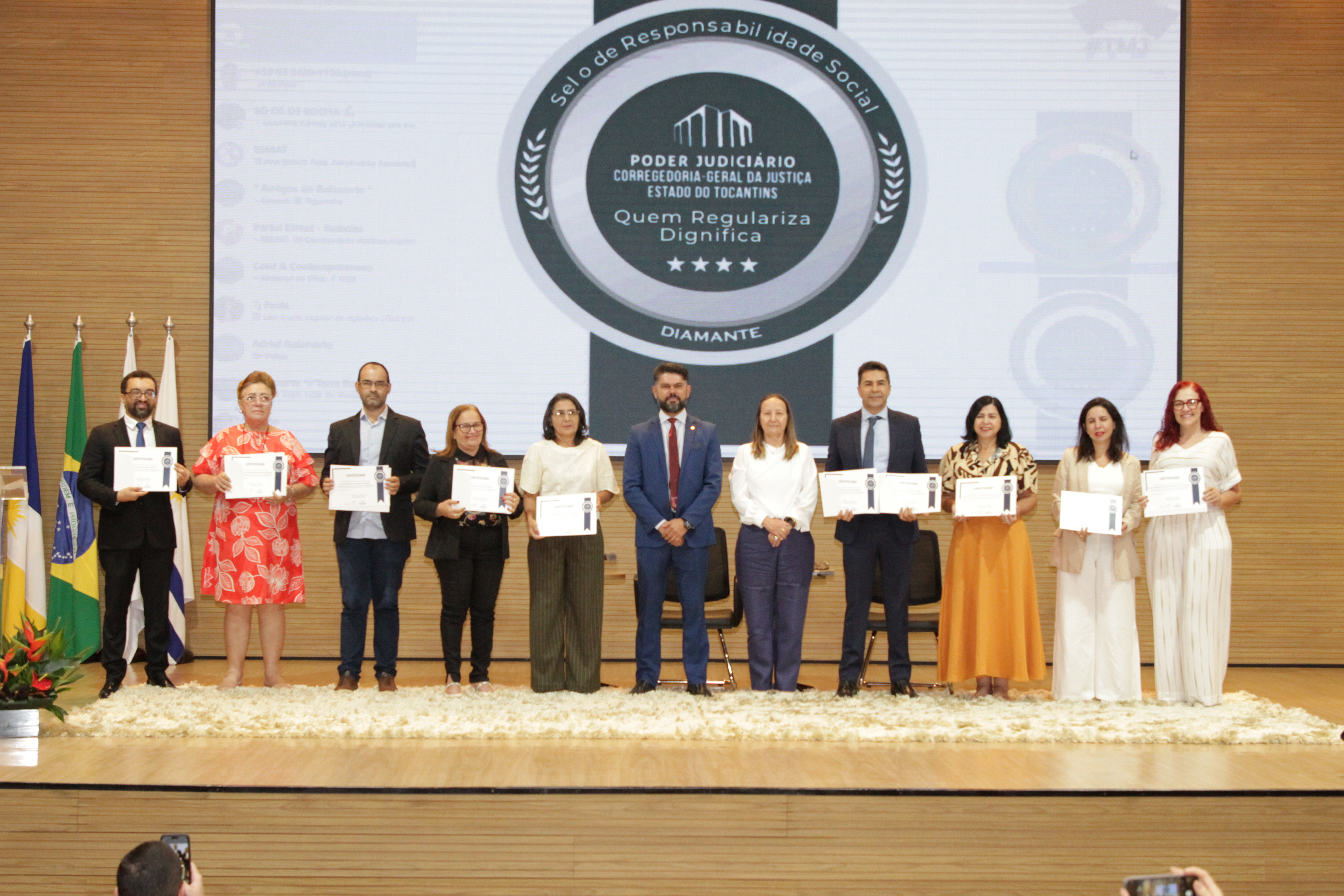 Fotografia colorida que mostra homens e mulheres no palco segurando um certificado