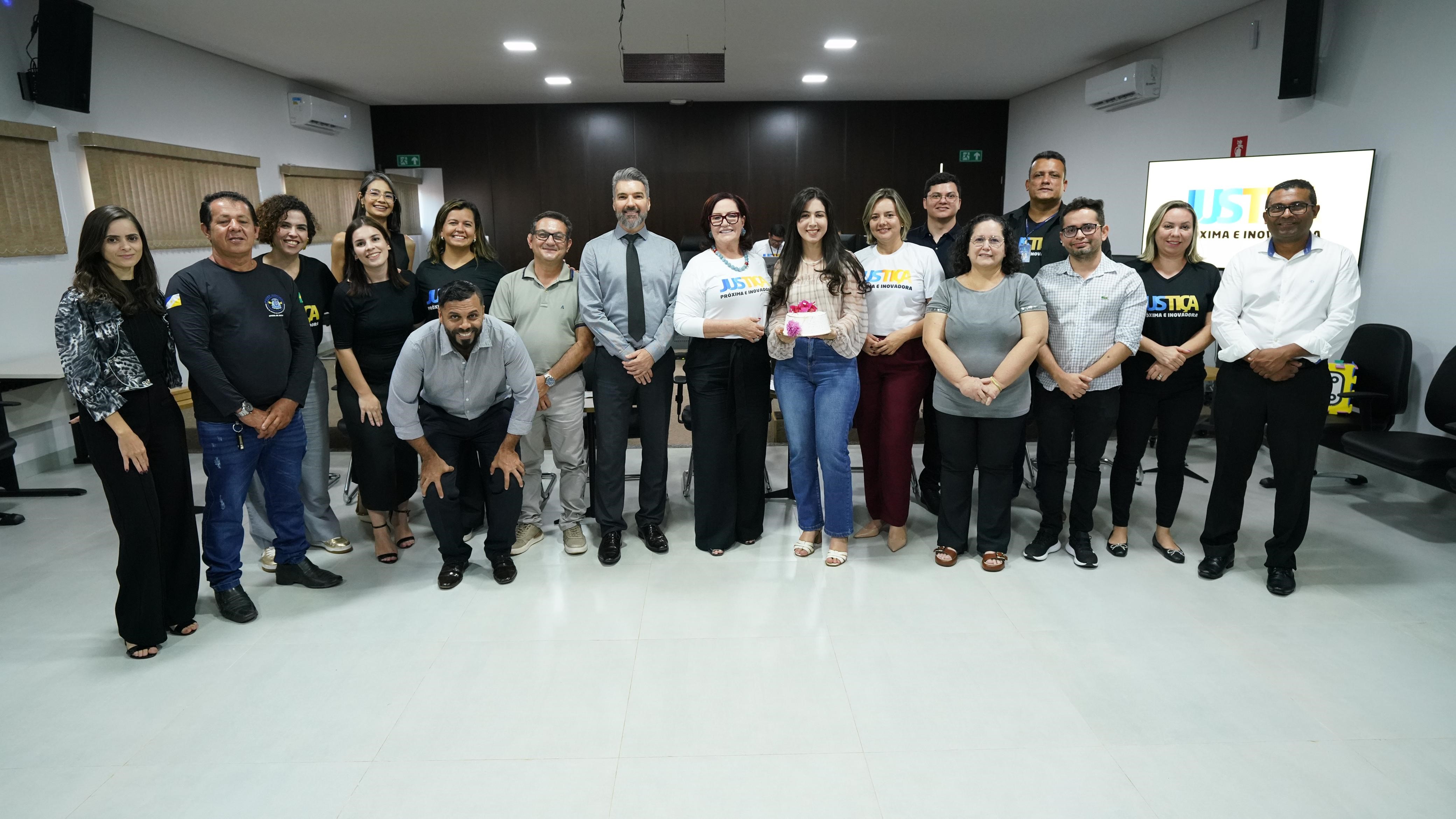 Fotografia que mostra homens e mulheres posando para a imagem e uma mulher branca, ao centro, segura um bolo. 