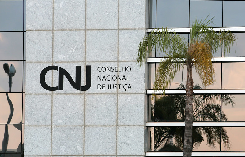 Fotografia colorida de uma parede com padrões quadrados e janelas espelhadas, onde na parede está escrito "CNJ- Conselho Nacional de Justiça"