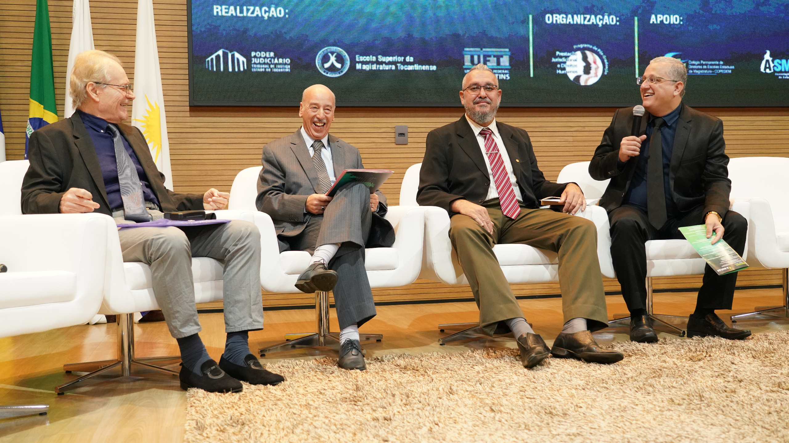 Fotografia colorida que mostra quatro homens brancos de terno e gravata sentados sorrindo durante apresentação no Congresso