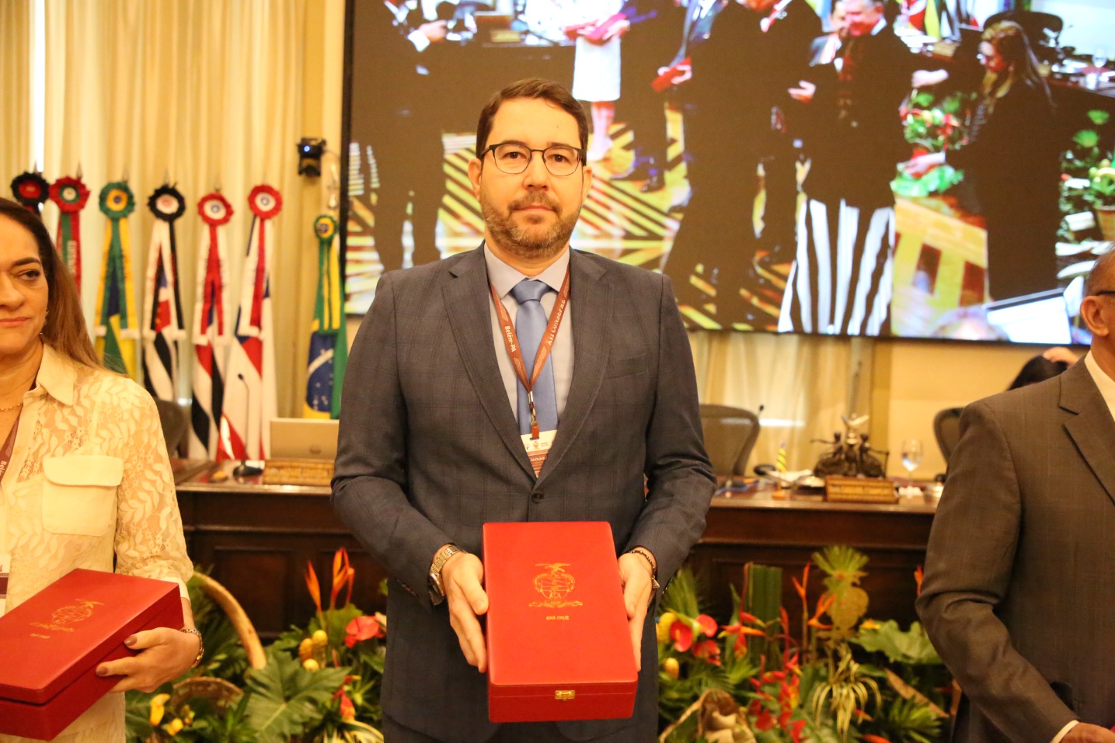 Imagem mostra um homem branco de barba  e óculos segurando uma caixa vermelha com a ordem do mérito