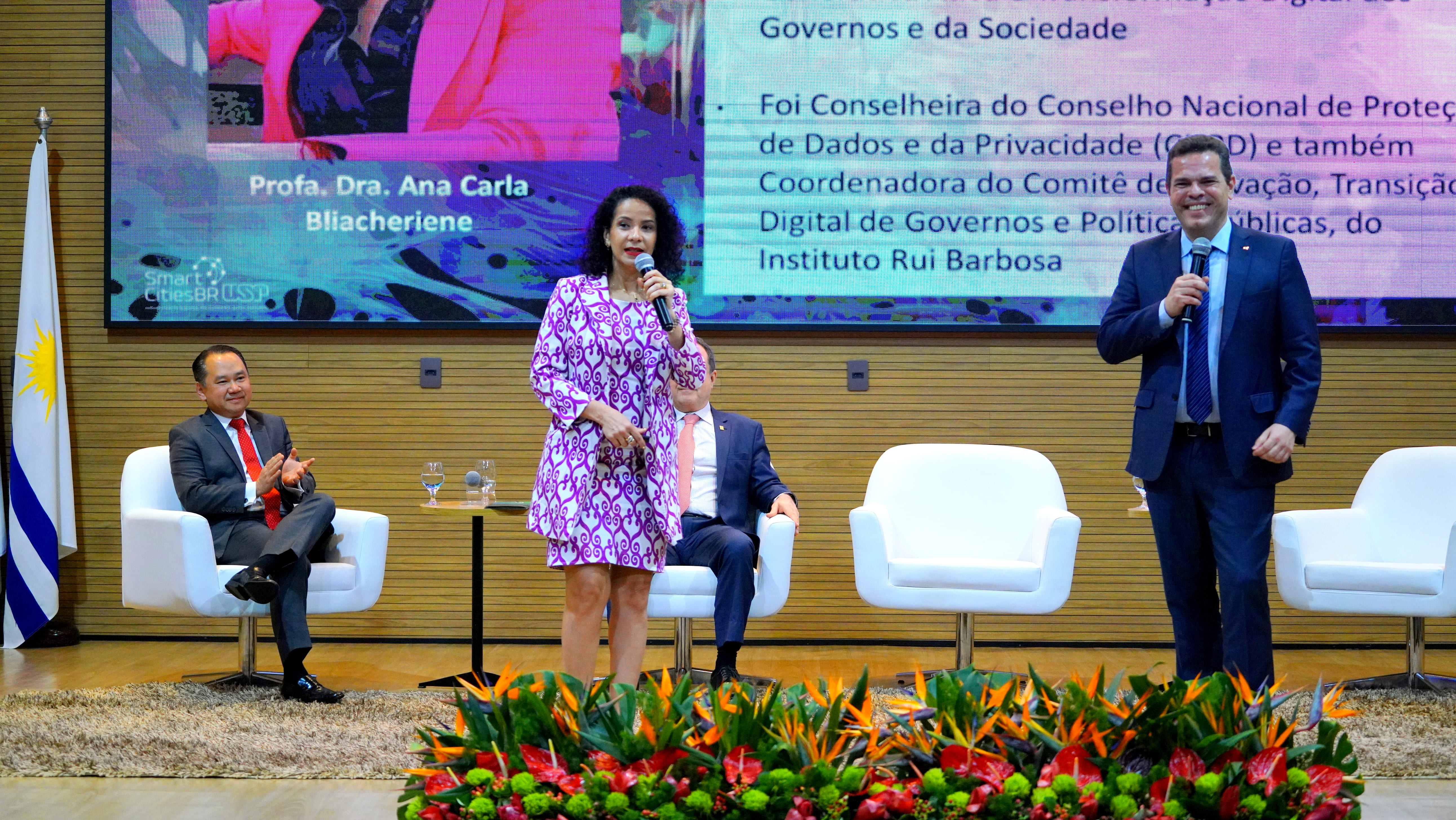 Imagem colorida que mostra um homem e uma mulher falando em um palco cujo fundo tem um telão azul sobre o Congresso Internacional dos Direitos Humanos