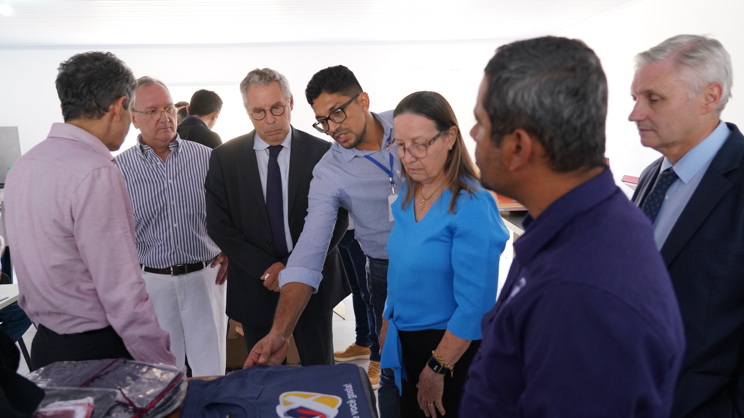Imagem colorida que mostra seis homens e uma mulher olhando uma malharia 