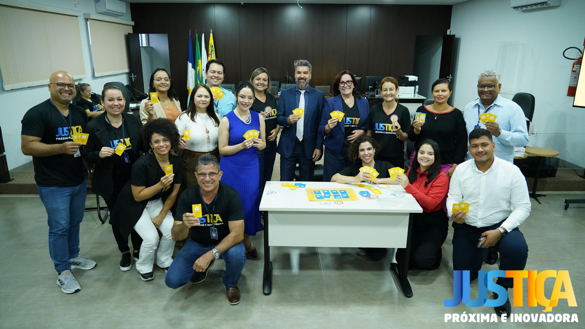 Fotografia colorida que mostra homens e mulheres, a presidente do TJTO, diretores,  servidores e o juiz da Comarca segurando um card e sorrindo pra foto