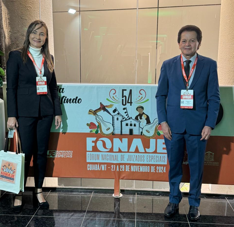 Fotografia colorida que mostra uma mulher e um homem posando pra foto em frente a um banner escrito Fonaje