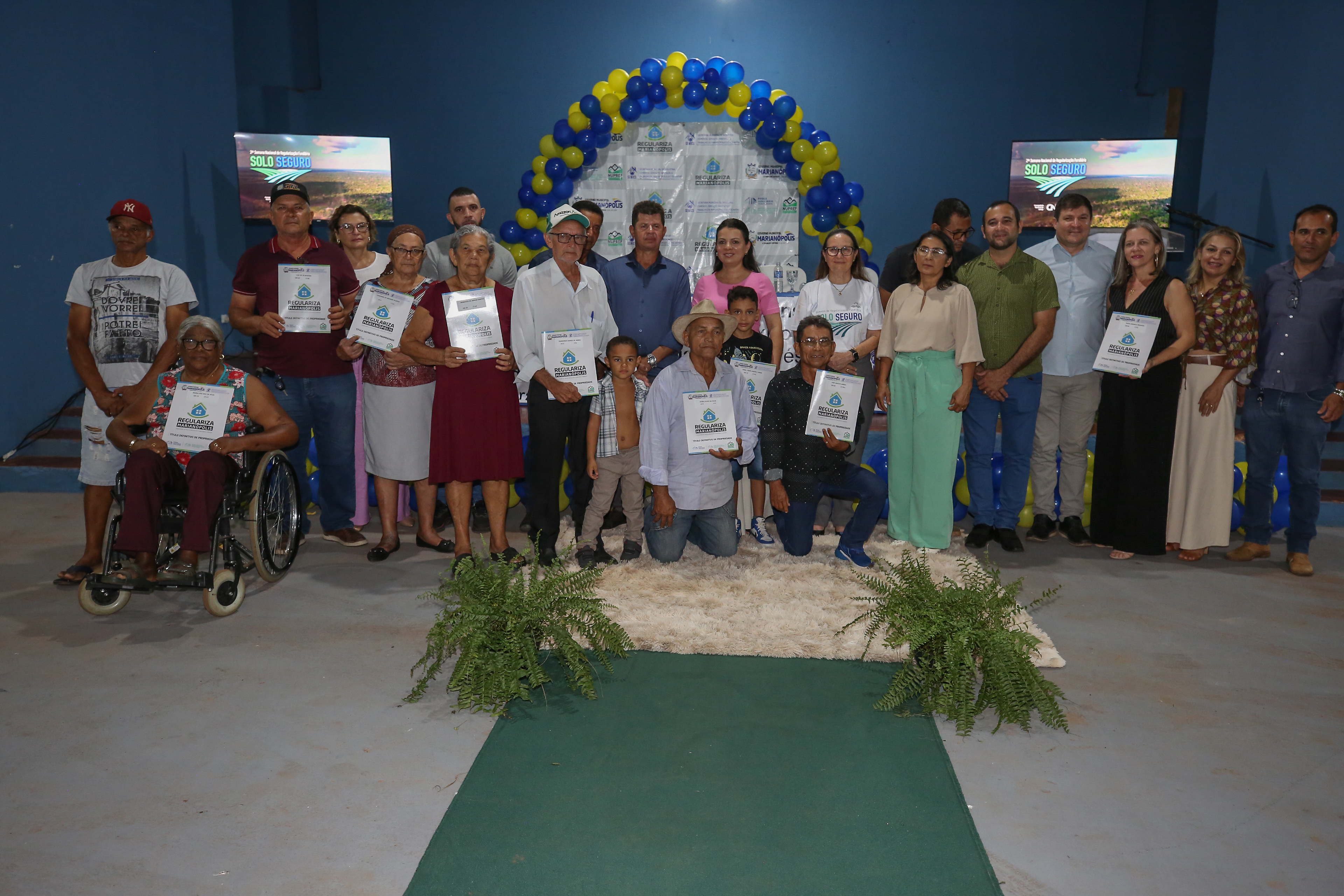 Fotografia colorida que mostram várias pessoas posando pra foto segurando título de posse de terra