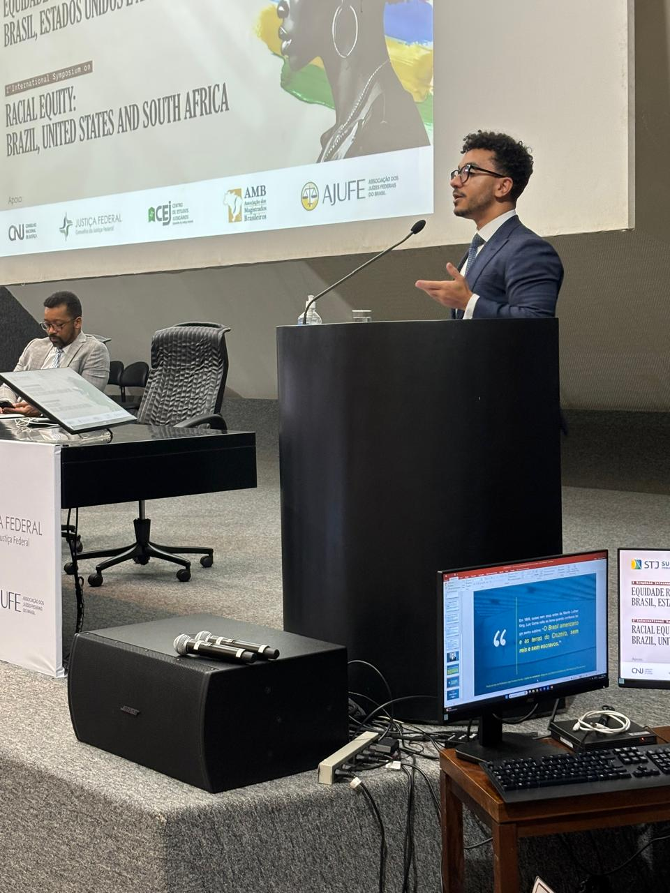 Imagem mostra dois participantes do I Simpósio Internacional pela Equidade Racial: Brasil, Estados Unidos e África do Sul, no Auditório Externo do Superior Tribunal de Justiça, um deles sentado à mesa e outro no púlpito