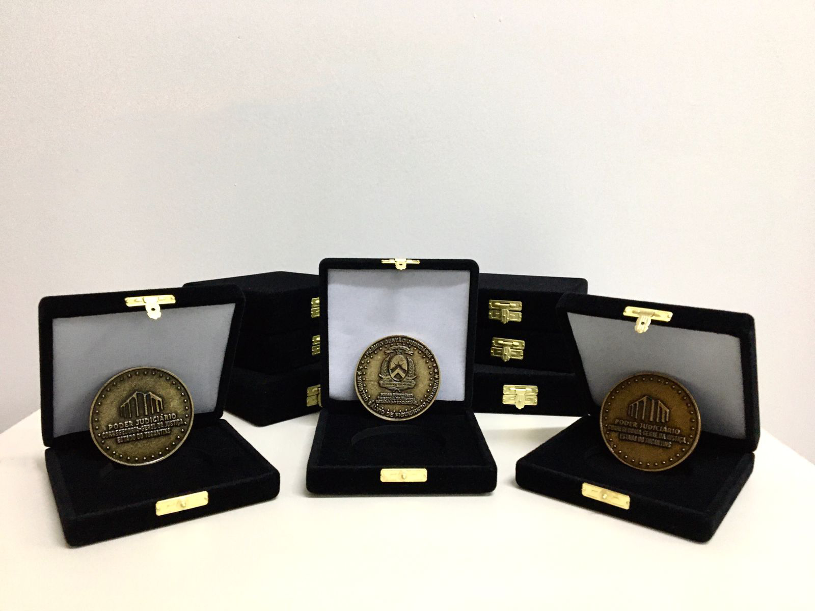 Fotografia de três medalhas tematizadas com os símbolos do Poder Judiciário, dentro de caixinhas pretas em cima de uma mesa branca 