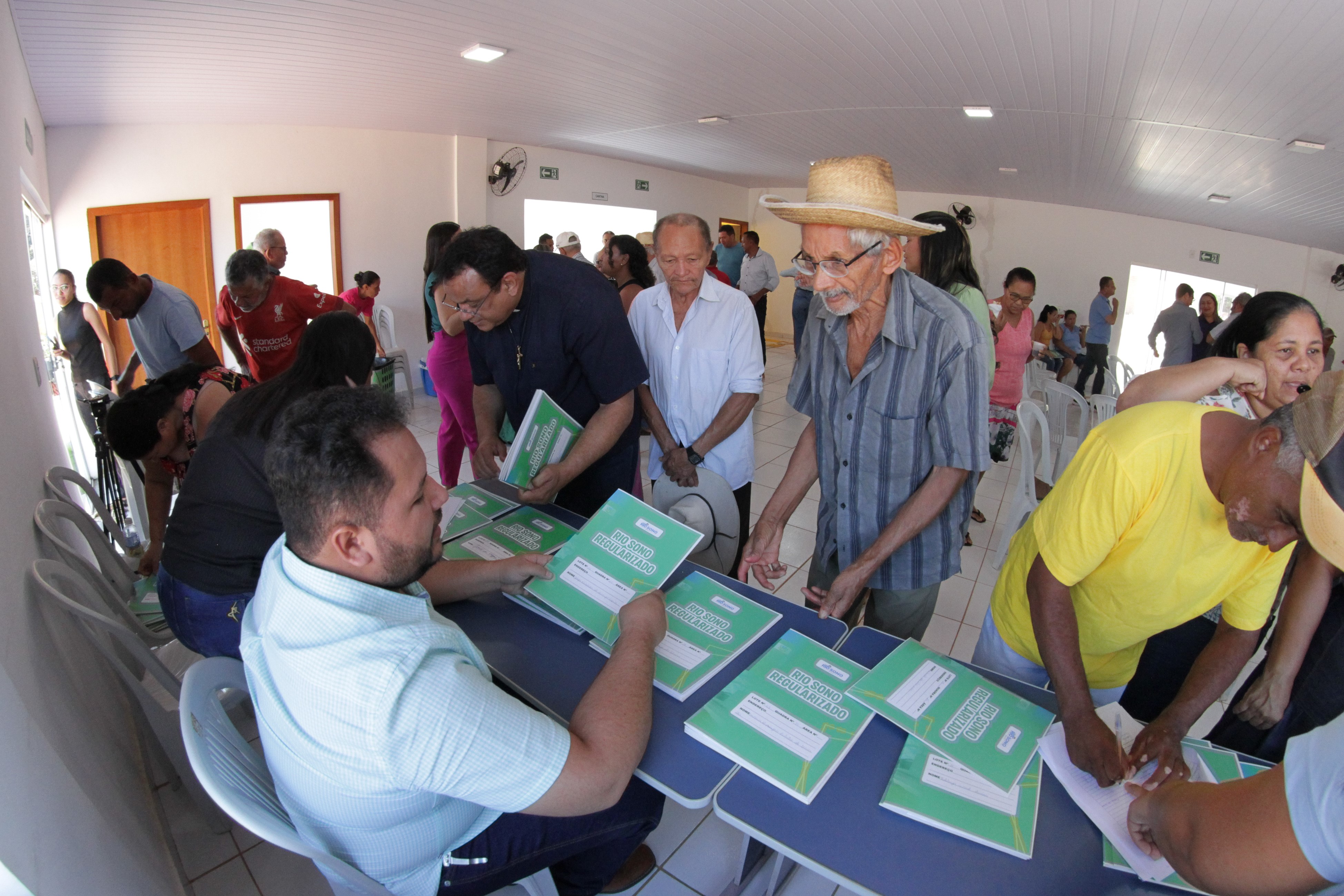 Imagem com diversas pessoas reunidas em uma sala e em pé aguardando para receber os títulos de suas propriedades