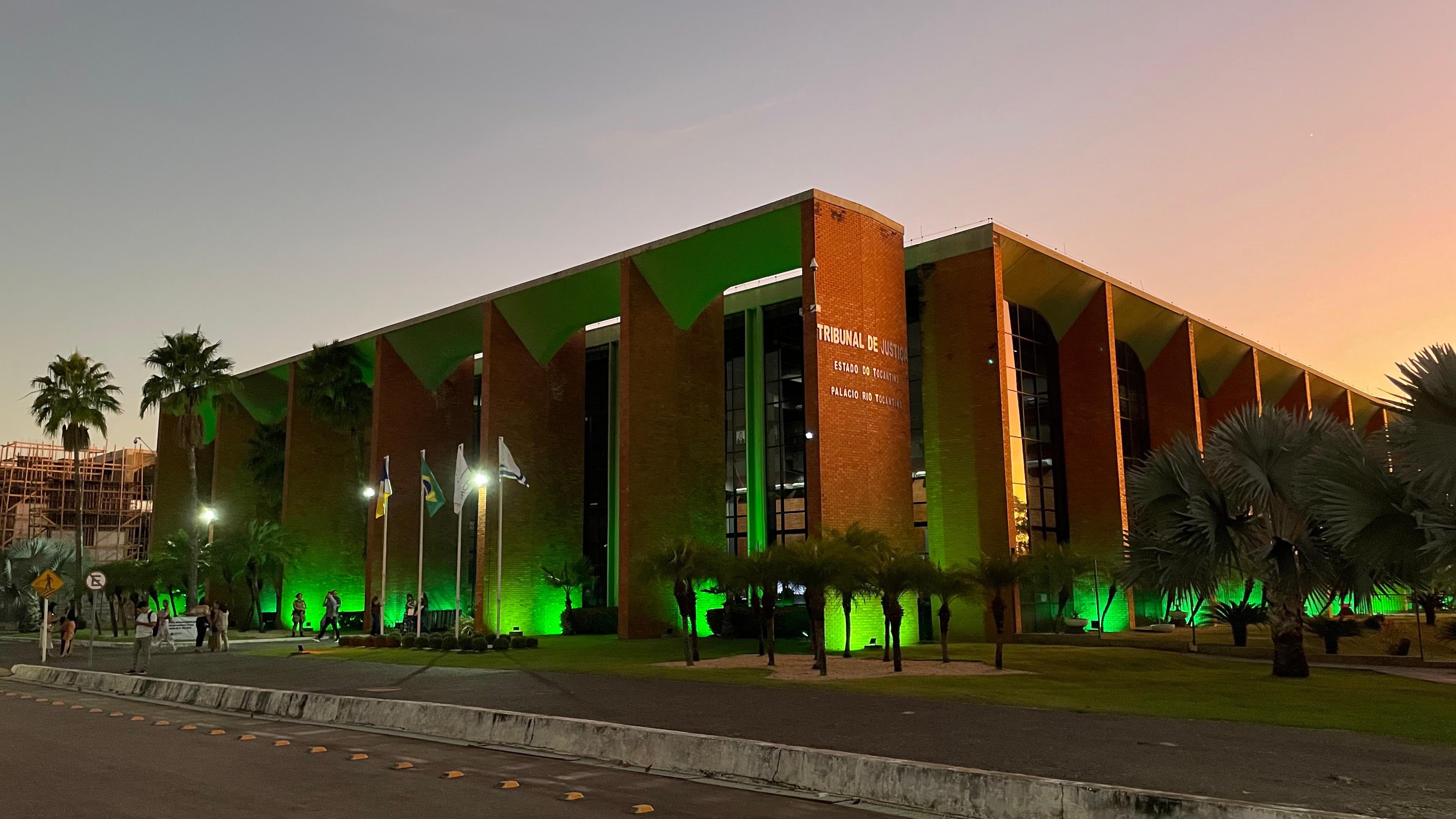 Faixada do prédio do TJTO iluminado na cor verde e a frente árvores verdes