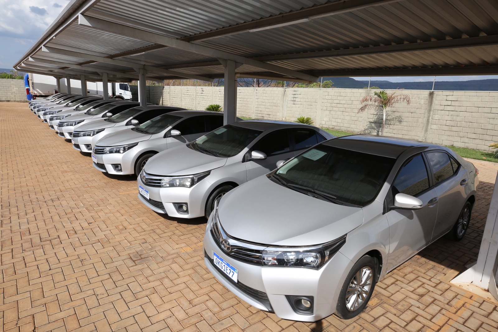 11 veículos de passeio na cor cinza expostos, alinhados, sob uma cobertura de garagem 