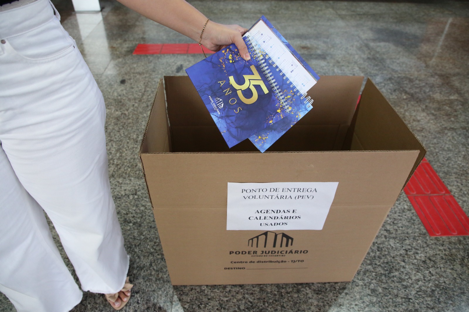 Mão depositando agenda azul dentro de caixa de papelão