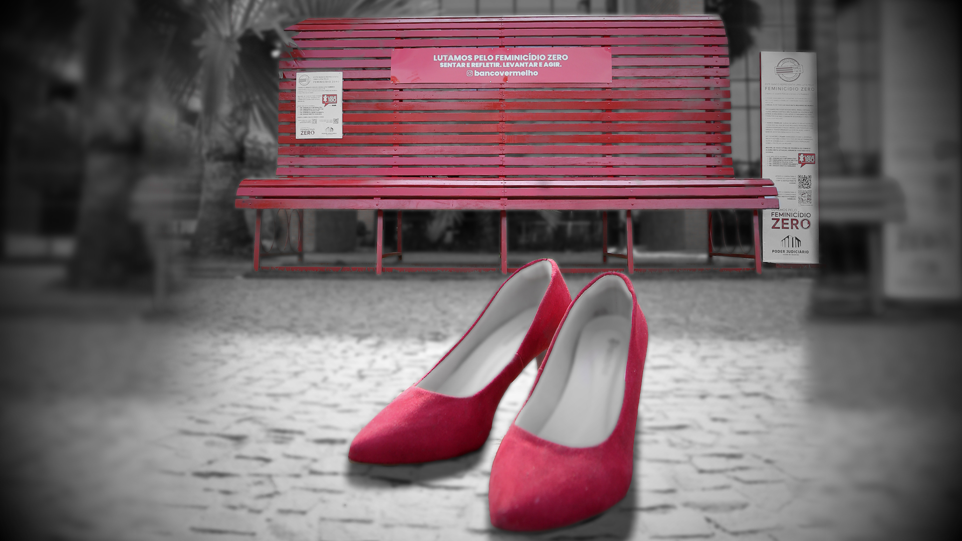 Um par de sapatos vermelhos femininos de salto alto em um caminho de pedras ao lado de um banco vermelho.