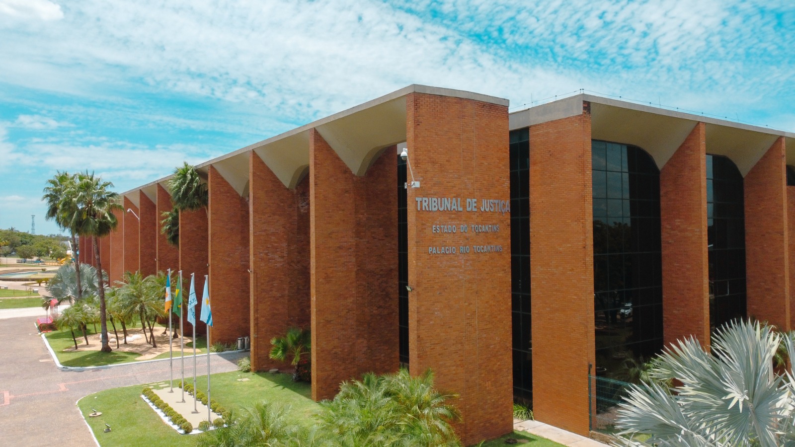 Na imagem aparece a vista panorâmica do prédio do Tribunal de Justiça do Tocantins, em Palmas. O edifício é de tijolos de cor avermelhada, com vegetação ao redor.